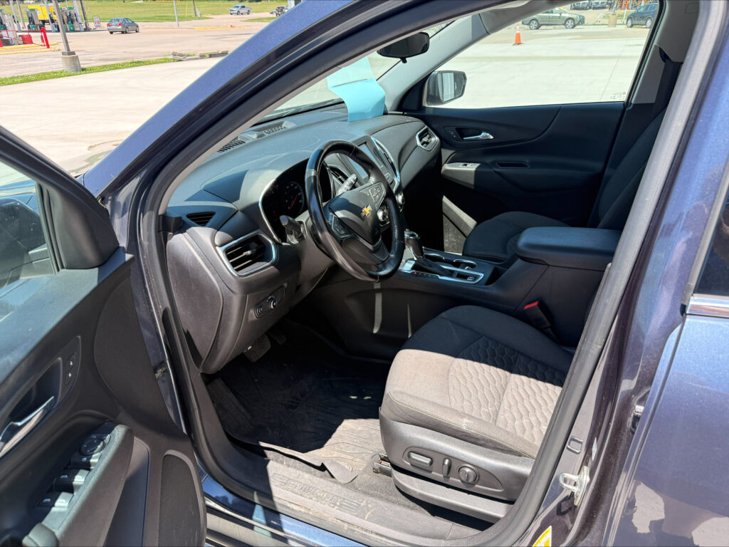 Interior of a Chevrolet SUV showing the steering wheel, center console, and a blue sticky note on the dashboard in front of the passenger seat.