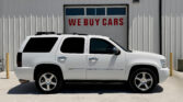White SUV parked in front of a building with a large garage door reading 'WE BUY CARS' in red letters.