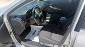 Interior of a car from the driver's side showing the steering wheel, dashboard, center console, and papers on the floor mat near the pedals