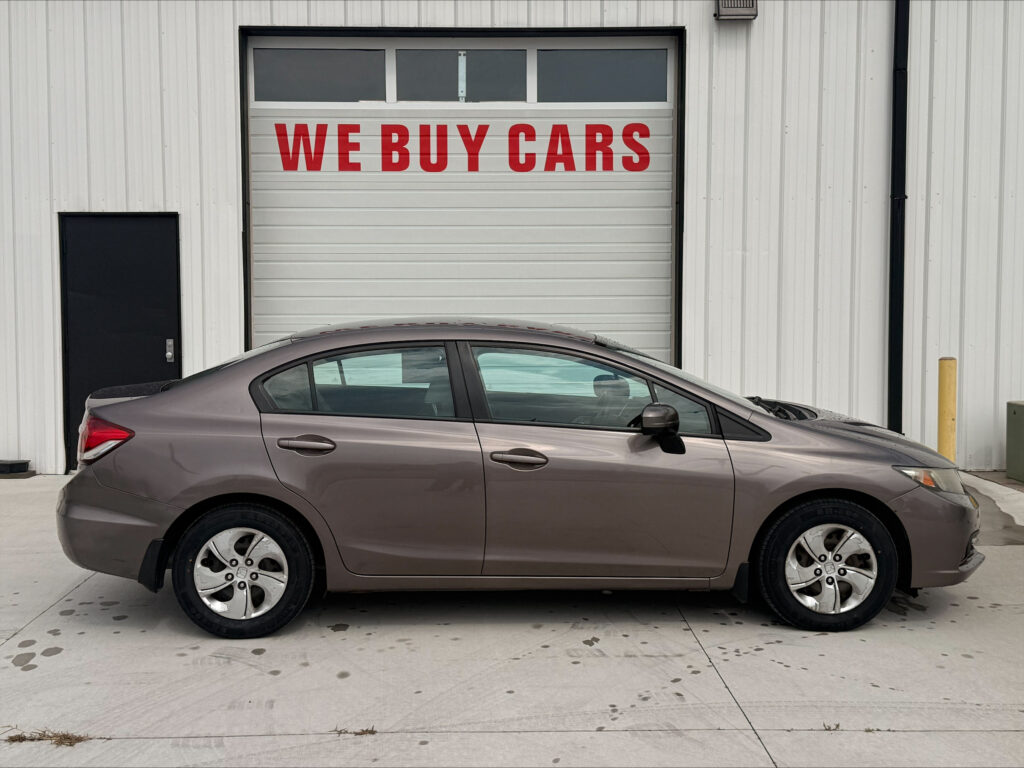 Gray sedan parked in front of a light-gray industrial garage door with a large red 'WE BUY CARS' sign above it.