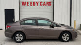 Gray sedan parked in front of a light-gray industrial garage door with a large red 'WE BUY CARS' sign above it.
