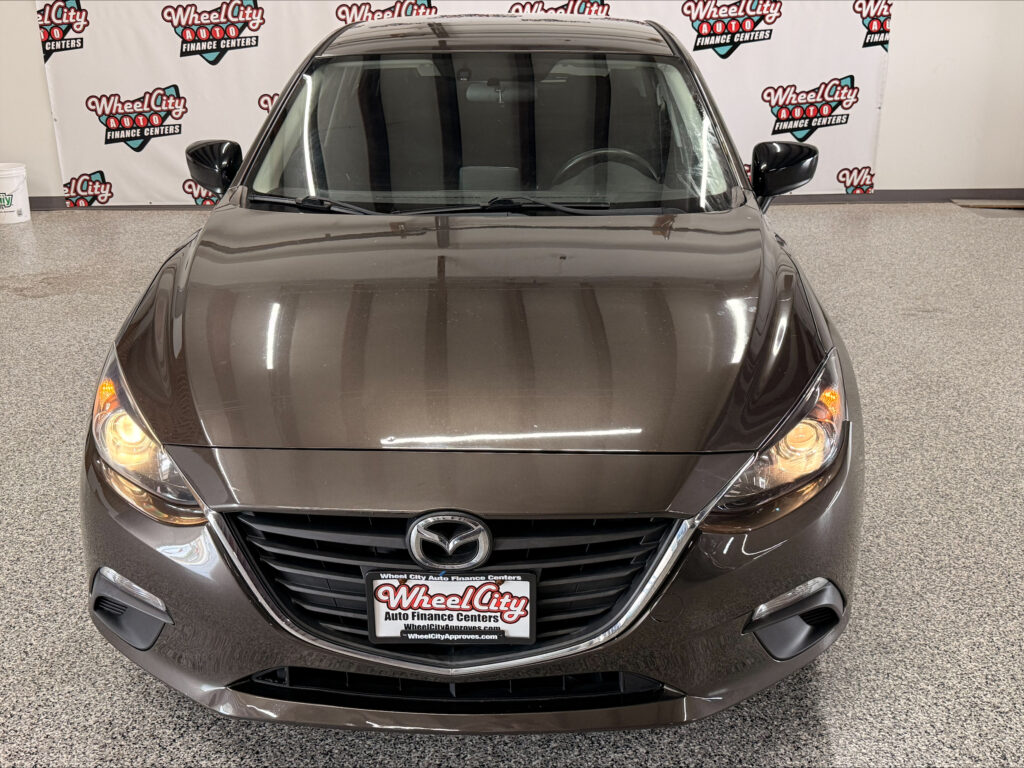 Front view of a brown Mazda SUV in a showroom with Wheel City Auto Finance Centers backdrop signage behind it.
