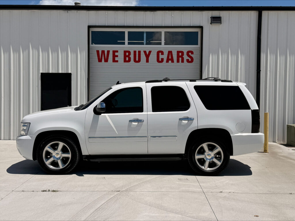 White SUV parked in front of a metal building with a garage door that reads WE BUY CARS.