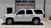 White SUV parked in front of a metal building with a garage door that reads WE BUY CARS.