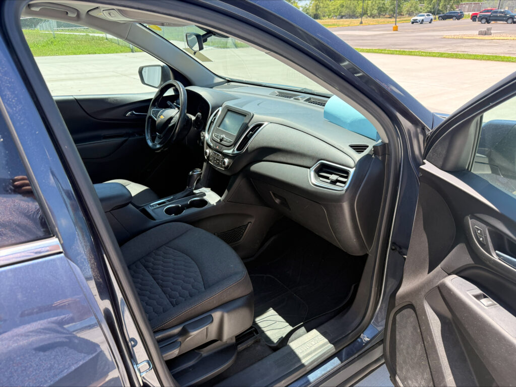 Open front driver-side door view of a Chevrolet car interior, showing steering wheel, center console, and dashboard.
