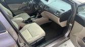 Interior view of a Honda sedan from the open front passenger door, showing beige cloth seats, steering wheel, center console, and dashboard.