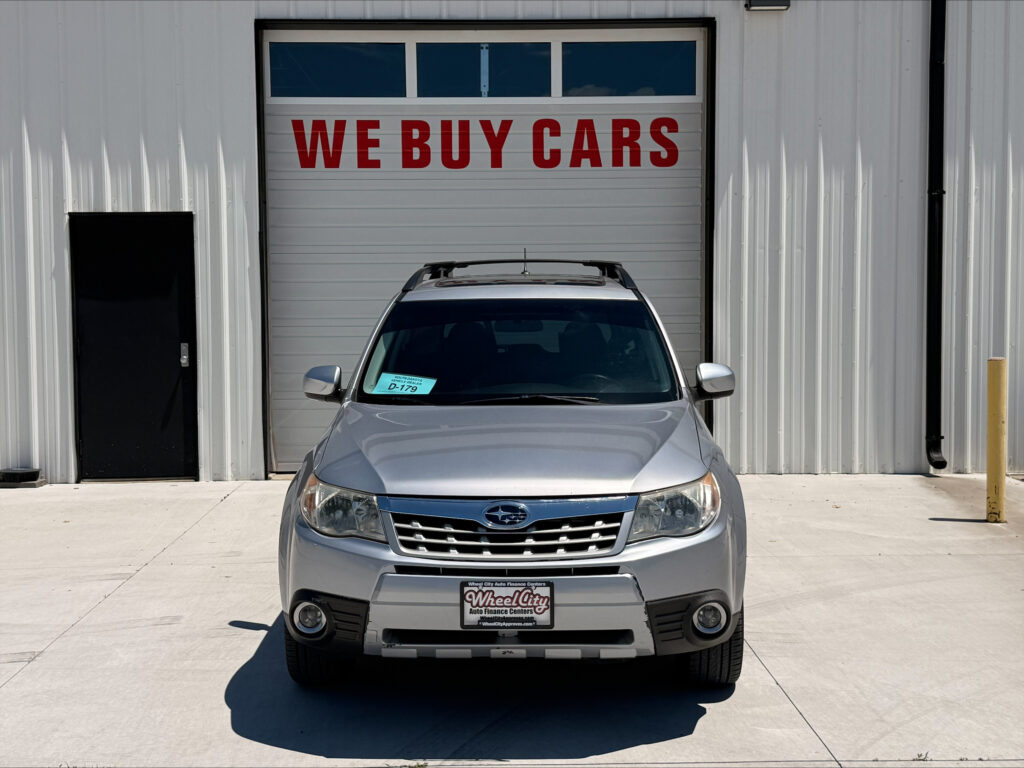 Silver SUV parked in front of a garage bay door with a red 'WE BUY CARS' sign above it