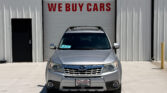 Silver SUV parked in front of a garage bay door with a red 'WE BUY CARS' sign above it