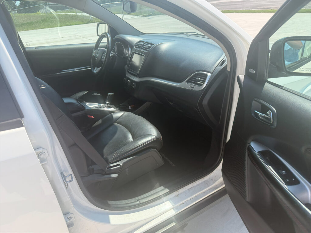 Interior view of a white SUV showing front seats, center console, and steering wheel from the open driver’s side door.