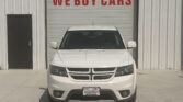 White Dodge SUV head-on in front of a garage door that says 'WE BUY CARS' in red letters.
