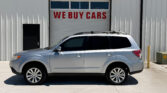 Silver SUV parked in front of a light-colored industrial building with a large garage door reading 'WE BUY CARS'.