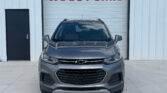 Front view of a gray Chevrolet SUV parked in front of a white building with a large red 'WE BUY CARS' sign on the door behind it.