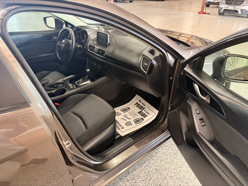 Interior of a car with the driver’s door open, showing the steering wheel, center touchscreen, gear shifter, and front seats.