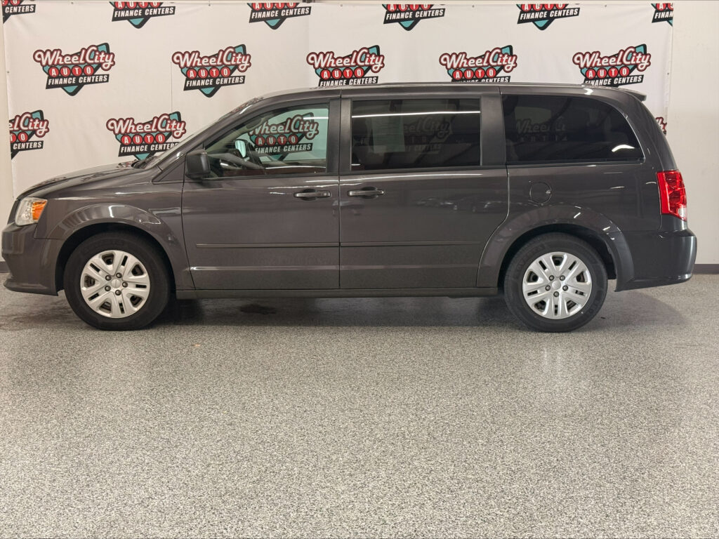 Side view of a gray minivan with sliding doors, parked indoors in front of Wheel City Auto Finance Centers banners.