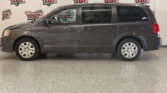 Side view of a gray minivan with sliding doors, parked indoors in front of Wheel City Auto Finance Centers banners.