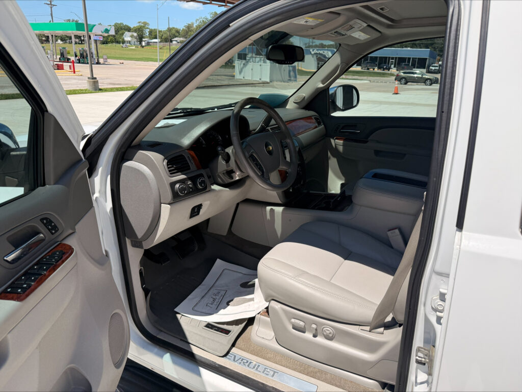 Open car door reveals the beige interior of a Chevrolet SUV, steering wheel and dashboard in view with a gas station outside the window.