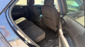 Inside rear passenger area of a blue car with black fabric seats and front seats visible, open rear door showing the parking lot outside.