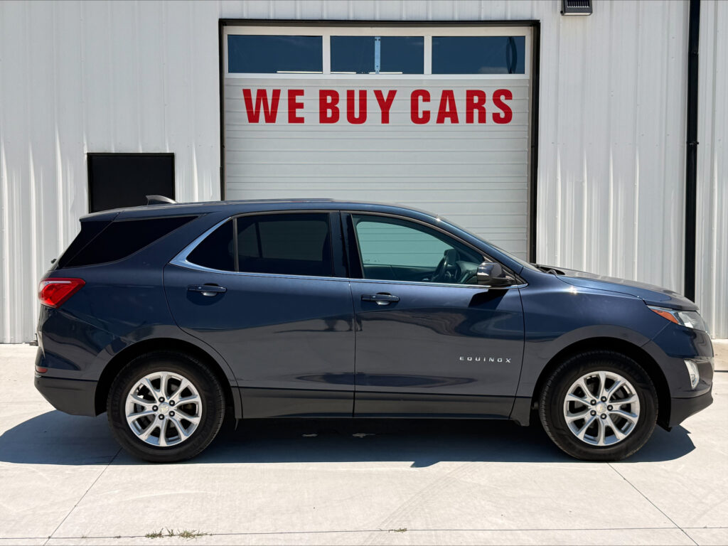 Dark blue Chevrolet Equinox parked in front of a white industrial building with a red WE BUY CARS sign on the garage door behind it.