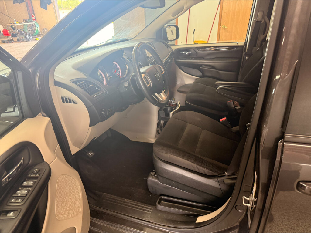 Interior of a vehicle cabin viewed from the open driver’s side door, showing the dashboard, steering wheel, and front seats