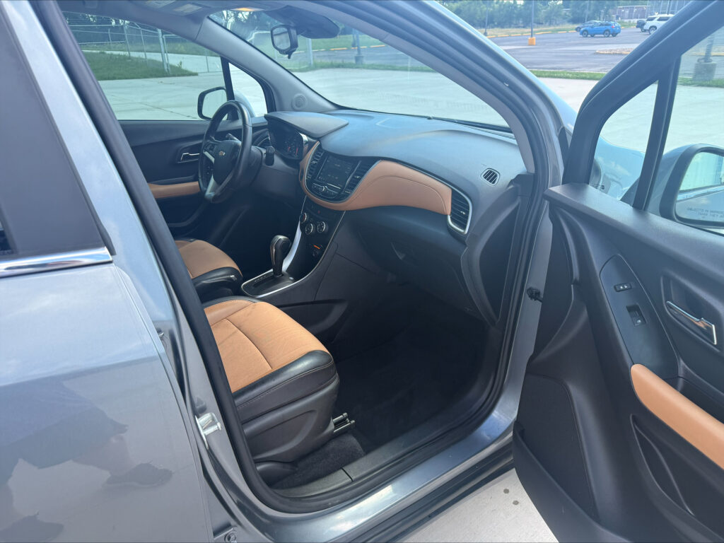 Interior of a gray SUV with brown leather seats and the driver’s door ajar, showing the steering wheel and center console with a touchscreen unlocked in a parking lot.