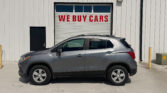 Silver SUV parked in front of a white metal building with a large garage door displaying 'WE BUY CARS' in red letters.