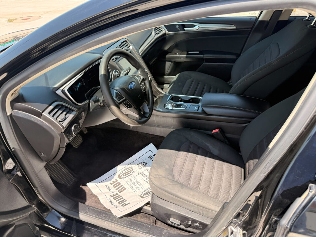 View of a Ford car’s black interior from the driver’s side, showing the steering wheel, dashboard, center console, and papers on the floor.