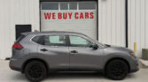 Gray SUV parked in front of a white metal warehouse with a garage door that reads 'WE BUY CARS'.
