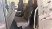 Interior of a gray minivan with two rows of black cloth seats visible through an open side door, headrests up.