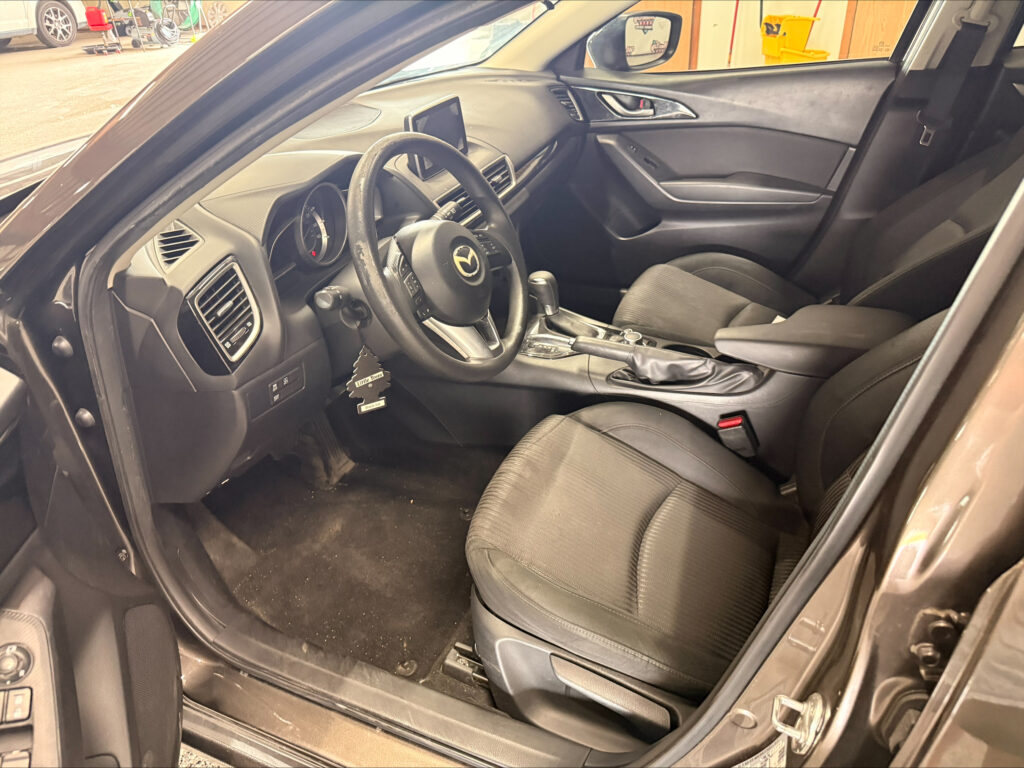 Interior of a Mazda with the driver's seat, steering wheel, and center console visible from the open front door.