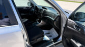 Interior of a silver SUV with the driver's seat, steering wheel, and center console visible through an open front door in a parking lot, with a person’s reflection in the window.