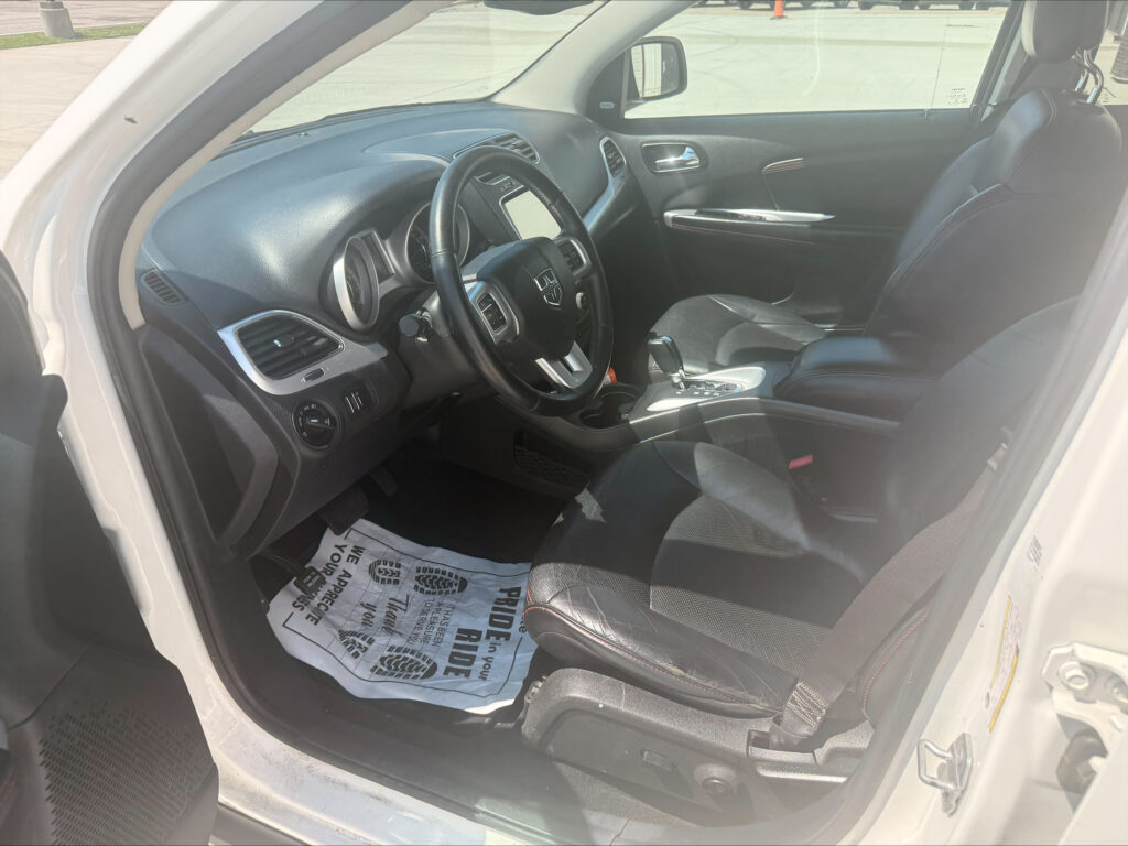 Interior of a car cabin: steering wheel, dashboard, and center console visible with a protective paper mat on the floor and the passenger seat in view, daytime light through the windows.