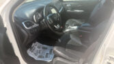 Interior of a car cabin: steering wheel, dashboard, and center console visible with a protective paper mat on the floor and the passenger seat in view, daytime light through the windows.