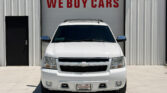 White SUV facing the camera in front of a building with a large red 'WE BUY CARS' sign above it
