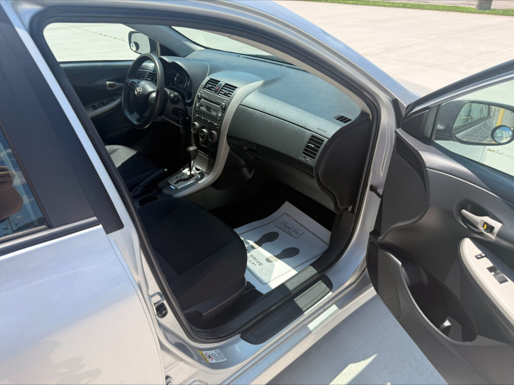 Interior of a silver car with the driver’s door open; steering wheel, dashboard, and gear shift visible.