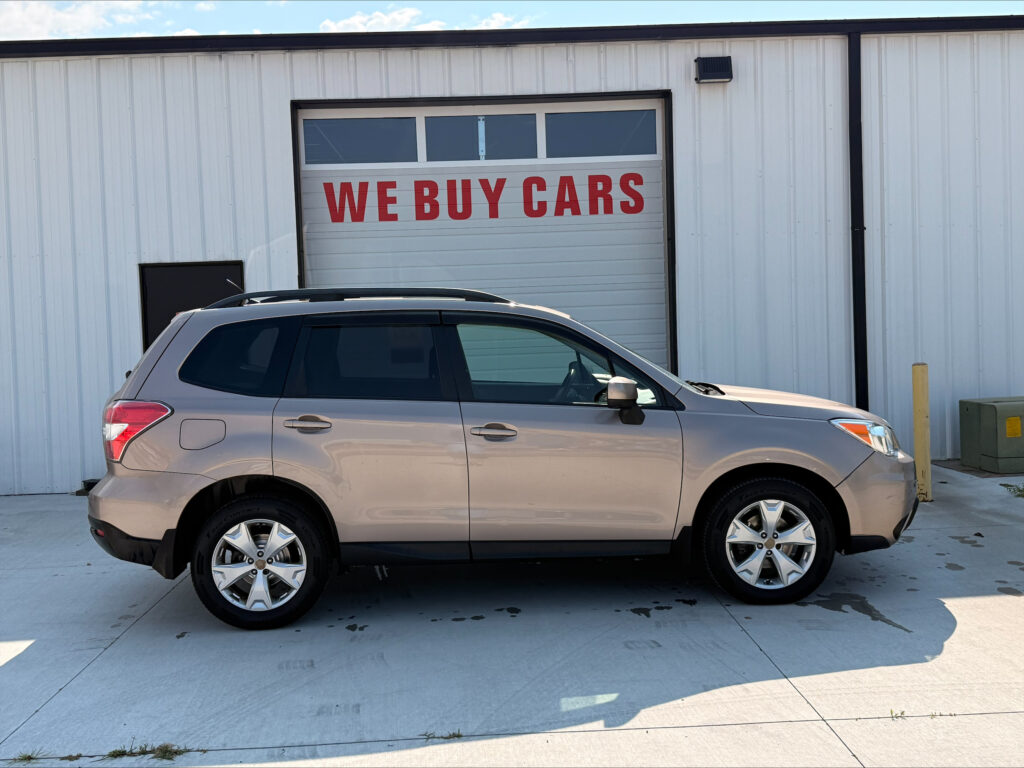 Silver SUV parked in front of a white industrial building with a large garage door reading 'WE BUY CARS' in red letters