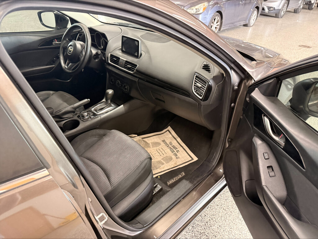 Open driver’s-side view of a dark car interior showing the steering wheel, center touchscreen, and gear shifter.