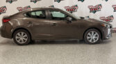 Brown four-door sedan indoors in a showroom with Wheel City Auto Finance Centers logos on a white backdrop behind it.