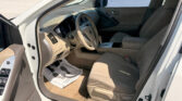 Open driver's door view of a beige SUV interior showing the steering wheel, dashboard, center console, and front seats; a parking lot is visible outside the windows.