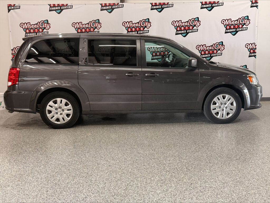 Side view of a gray minivan indoors, with a Wheel City Auto Finance Centers banner in the background.