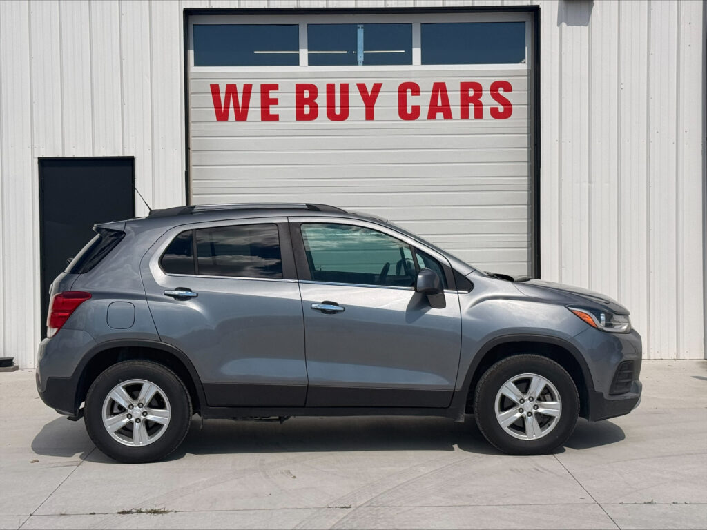 Silver SUV in front of a white warehouse with a large red WE BUY CARS sign on the garage door