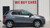 Silver SUV in front of a white warehouse with a large red WE BUY CARS sign on the garage door