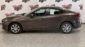 Brown mid-size sedan photographed indoors in front of a Wheel City Auto Finance Centers backdrop, shown from the passenger side with visible windows, door handles, and rear taillight.