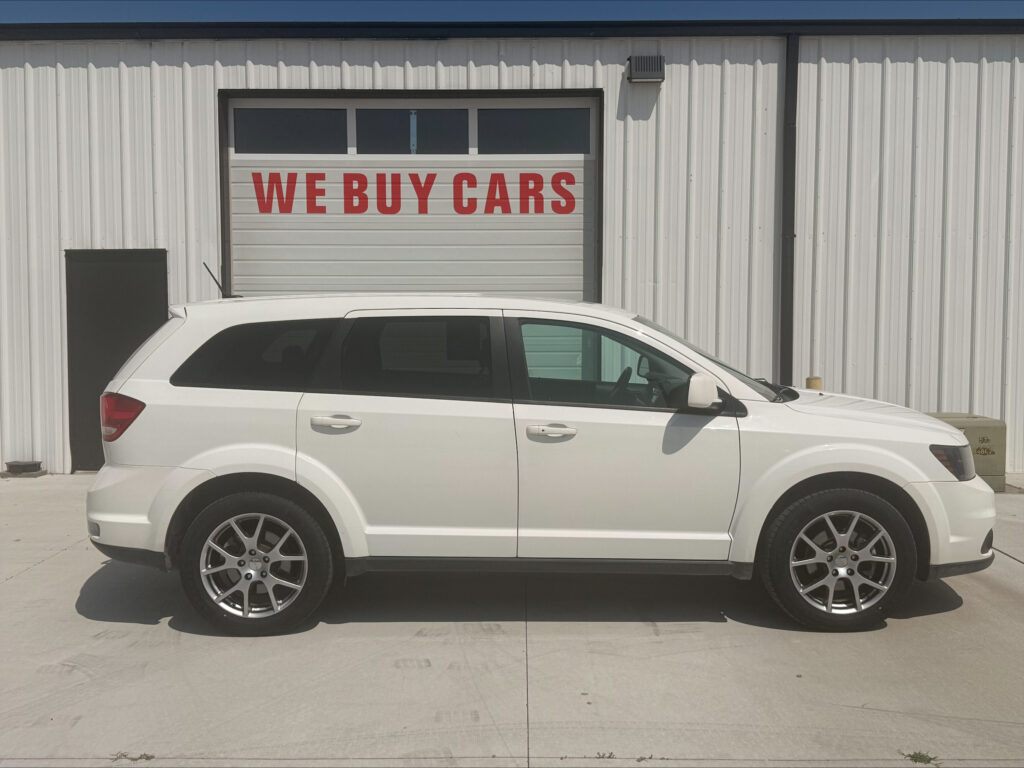White SUV parked in front of a building with a large garage door that says 'WE BUY CARS' in red letters on the door.