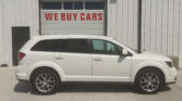 White SUV parked in front of a building with a large garage door that says 'WE BUY CARS' in red letters on the door.