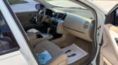 Interior of a white Nissan Murano with beige seats and center console visible, driver’s-side door open and dashboard in view; dealership floor mats on the front passenger side.