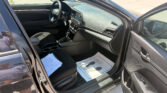 Interior of a dark gray car with the driver’s seat, steering wheel, center console and dashboard visible; papers lie on the front passenger seat and the door is open on the left side.