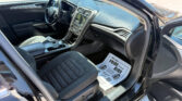 Interior of a car shows driver and passenger seats, steering wheel, center console, and paper floor mat visible on the passenger side