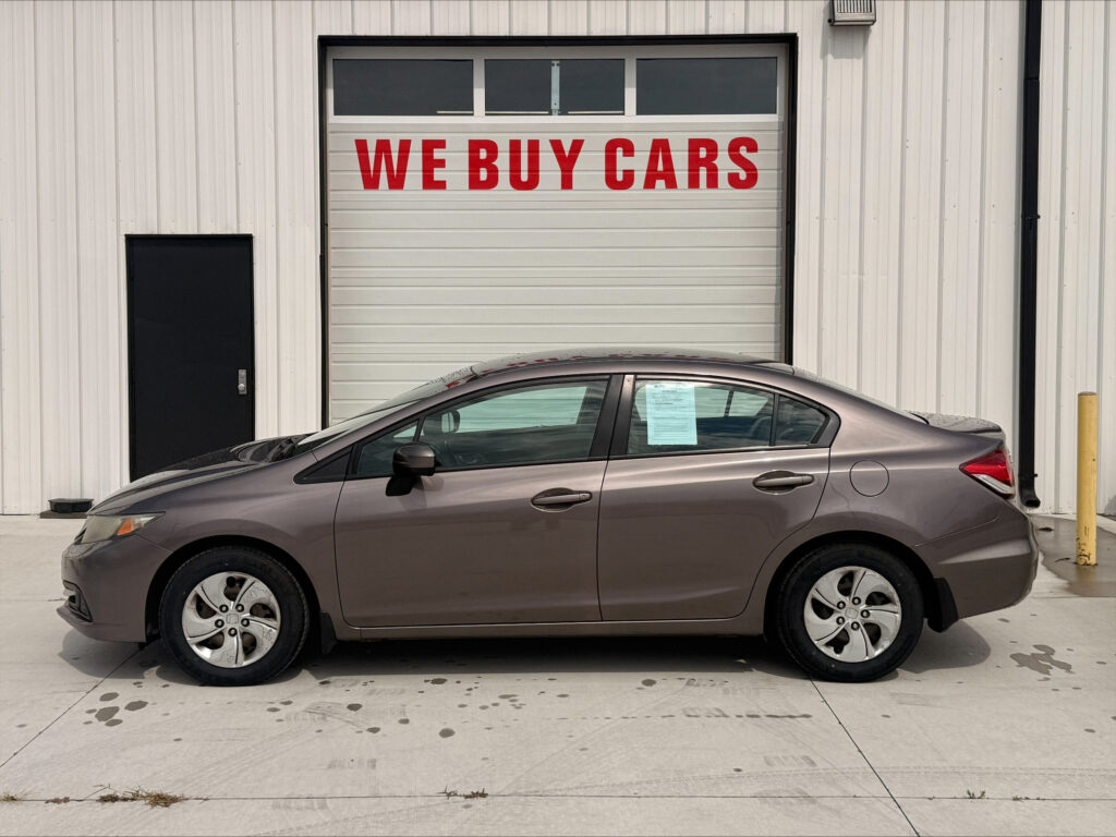 Gray sedan parked in front of a building with a large white garage door that reads 'WE BUY CARS'.