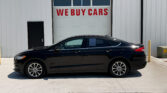 Black sedan parked in front of a white industrial building with a large door that reads 'WE BUY CARS' in red letters above the windowed section.