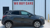 Gray SUV parked in front of a white industrial building with a garage door that reads 'WE BUY CARS'.